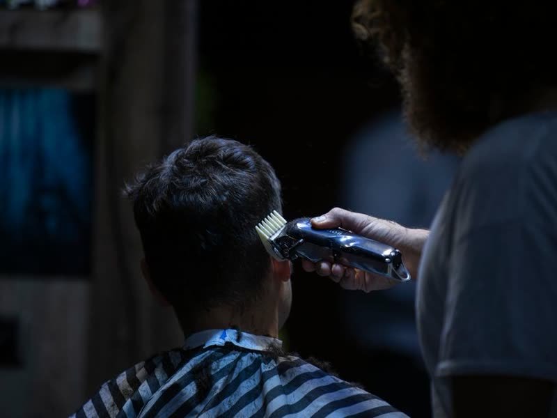 Barbeiro passando a máquina no cabelo de um cliente sentado na cadeira