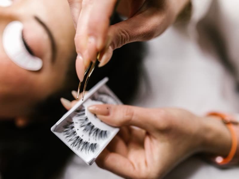 Profissional aplicando extensão de cílios com pinça, com a cliente de olhos fechados