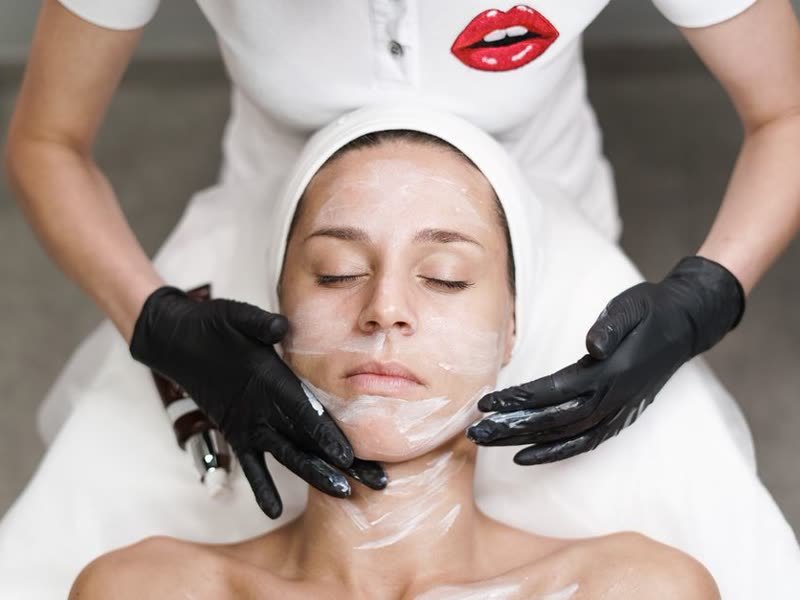 Esteticista aplicando máscara no rosto de uma cliente deitada na maca