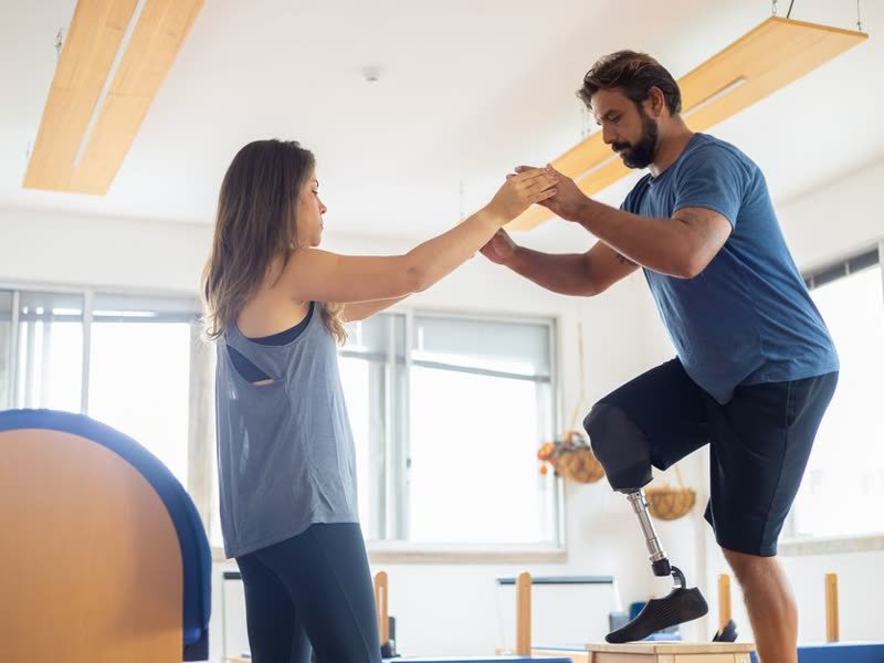 Fisioterapeuta apoiando um paciente com prótese durante um exercício