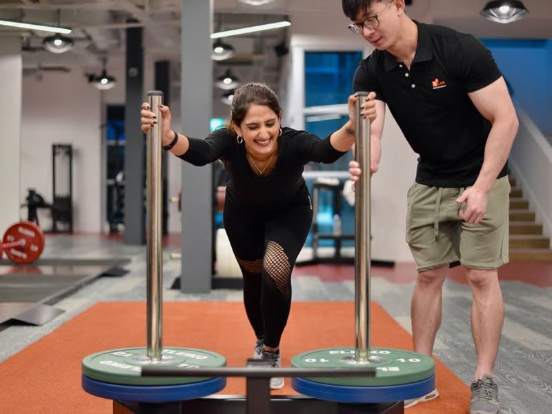 Personal trainer acompanhando uma aluna num exercício de equilíbrio na academia