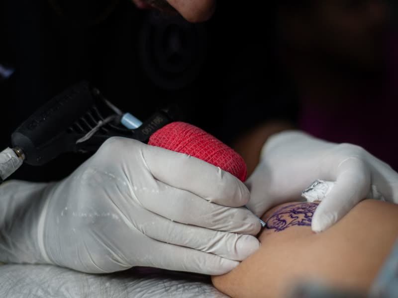 Tatuador com luvas trabalhando com a máquina na pele do cliente